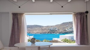 A room with a round table and four stools, a view of a coastal landscape with buildings and a blue sea. - Luxury Sea View Apartment w shared pool (Mykonos)