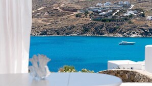 A coastal view with white buildings on a hillside, a clear blue sea, and a yacht in the distance. - Luxury Sea View Apartment w shared pool (Mykonos)