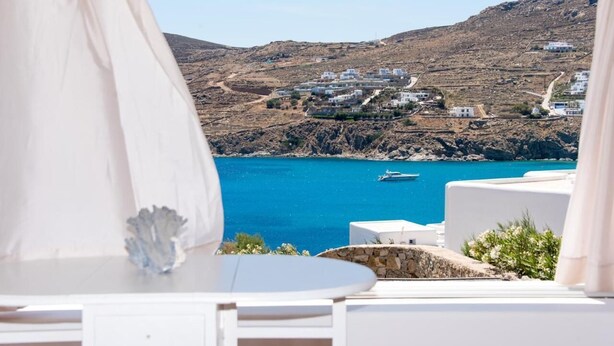 A coastal view with white buildings, a clear blue sea, and a boat in the distance. - Luxury Sea View Apartment w shared pool (Mykonos)