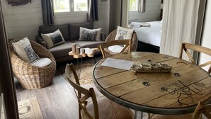 A cozy room with a wooden table, wicker chairs, a sofa with cushions, and a bed with white linens.