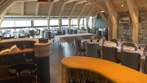 A spacious restaurant with high wooden ceilings and large windows. Tables are set with wine glasses and plates.