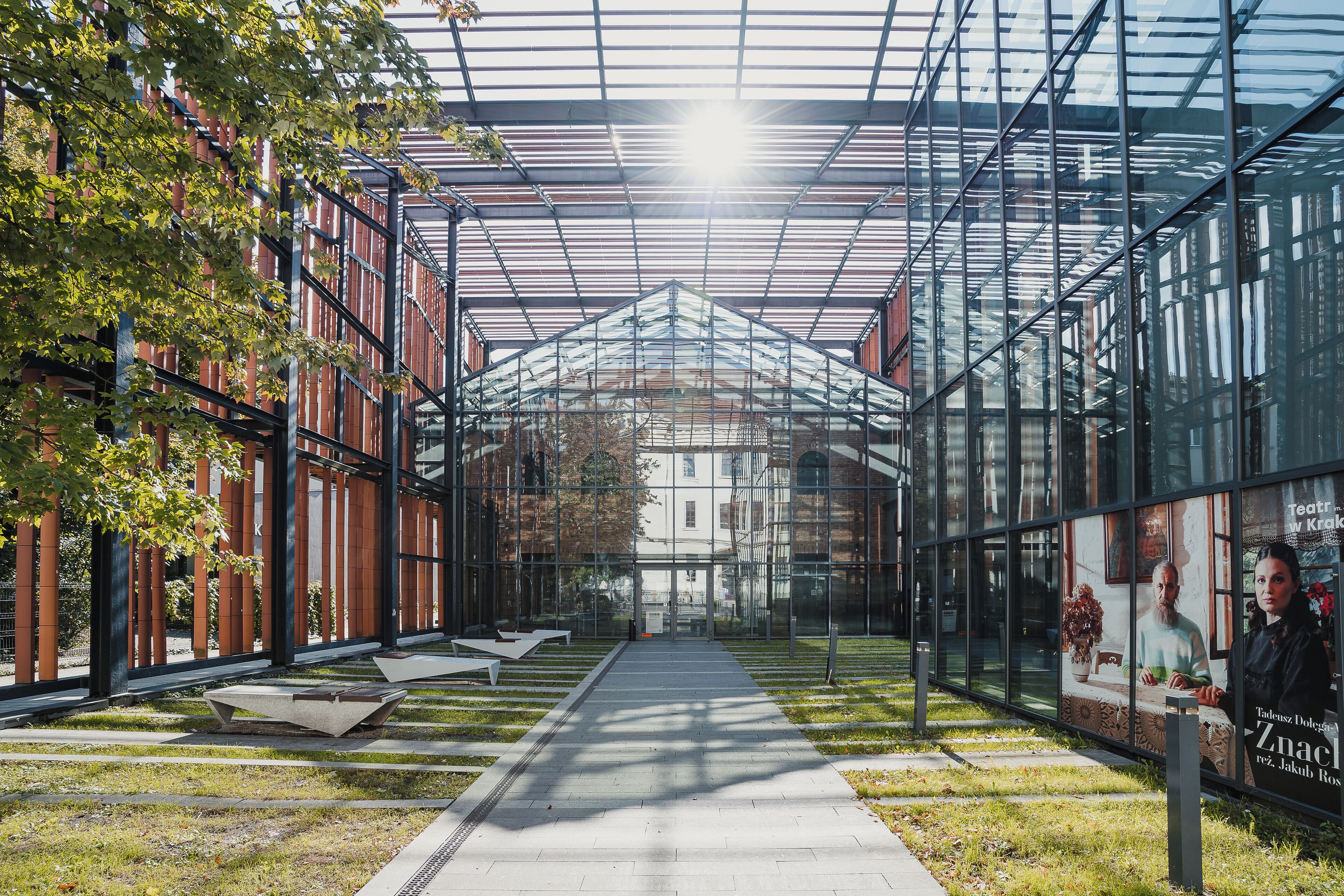 A modern building with a glass facade, a central walkway, and seating areas.