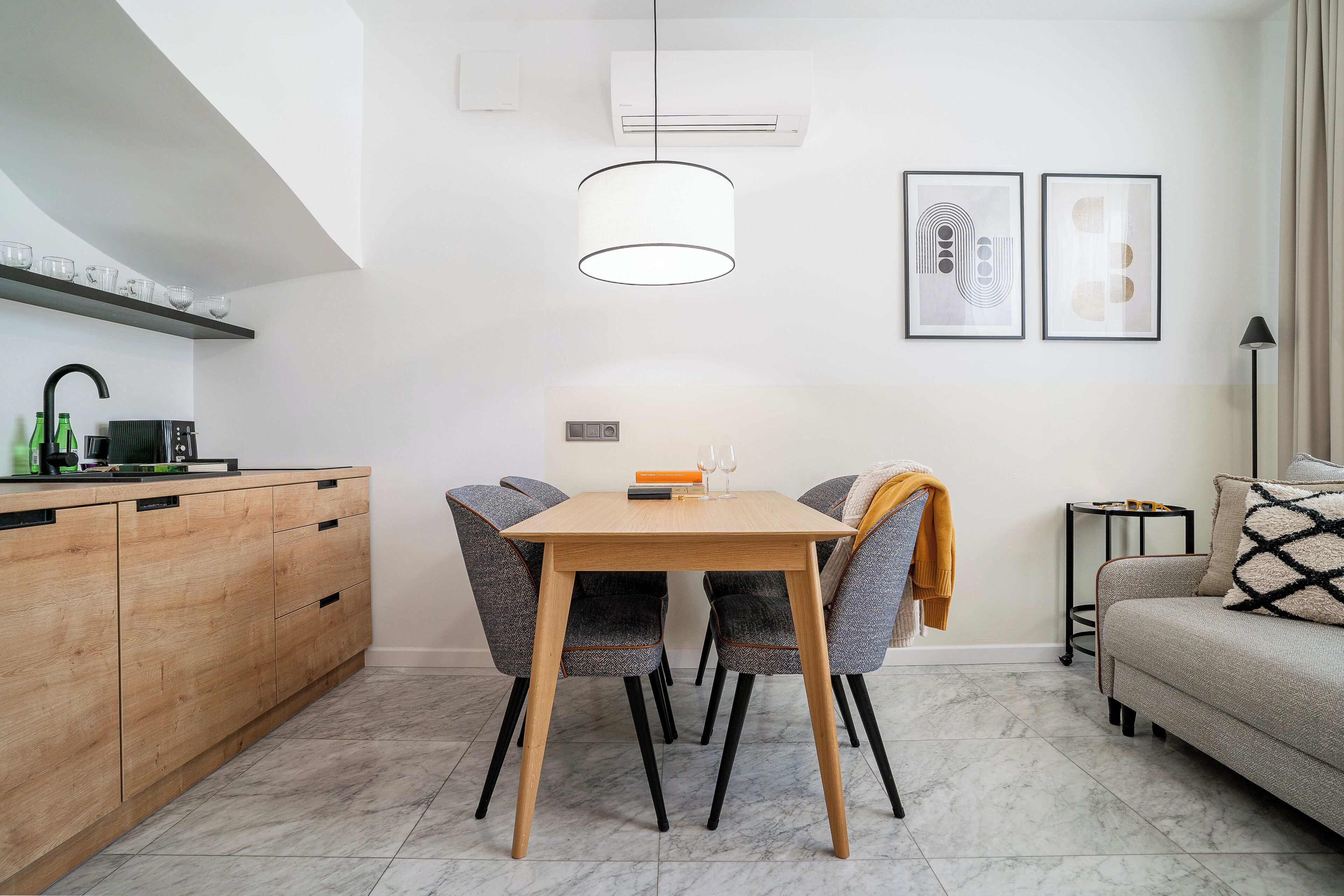 A modern kitchen with a wooden table and chairs, a hanging light fixture, and a built-in oven.