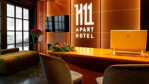 A hotel reception desk with a Dell computer, a potted plant, and a sign that reads "H11 Apart Hotel". - H11 Aparthotel (Kraków)