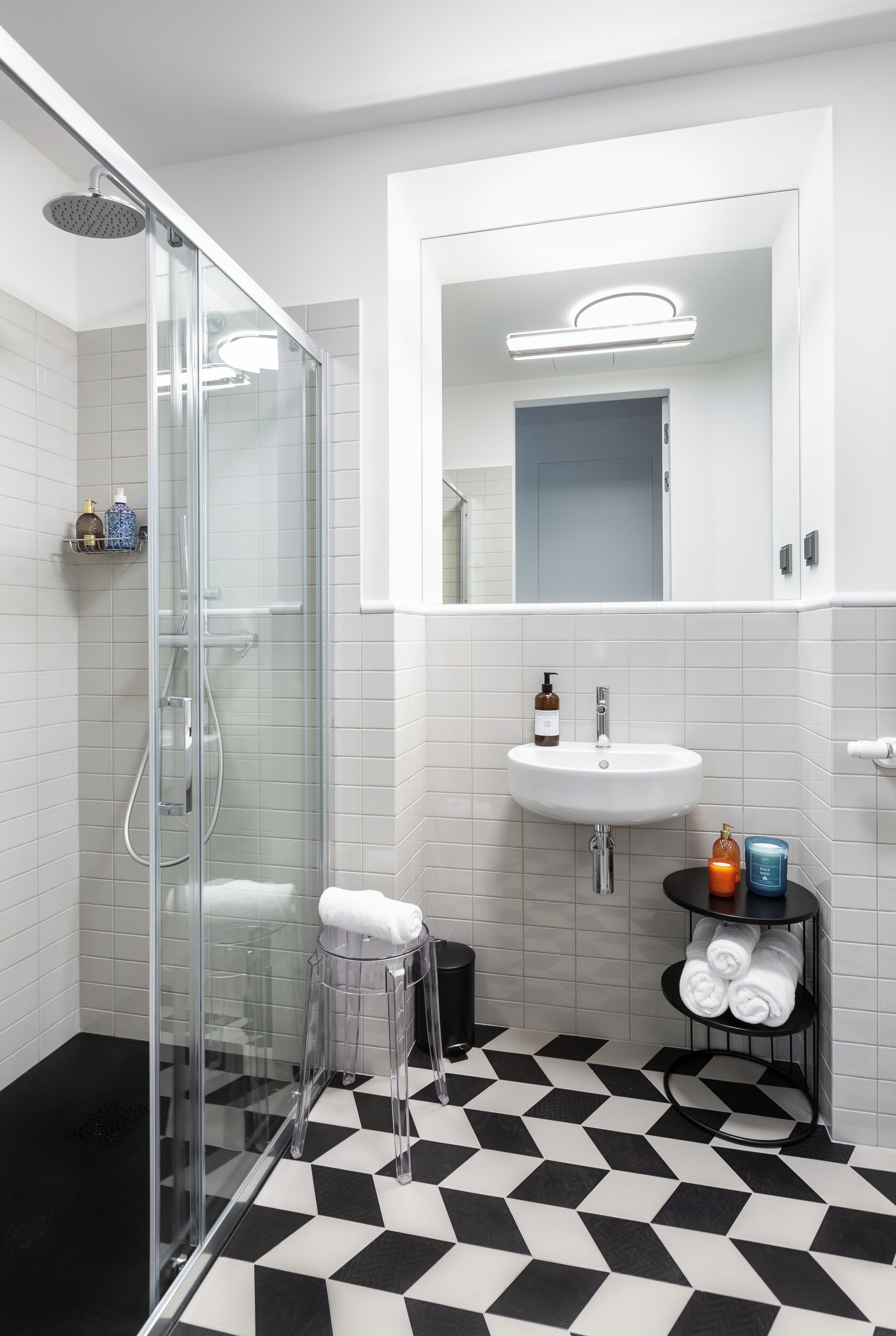 A modern bathroom with a glass shower enclosure, a white sink, and a black and white checkered floor.