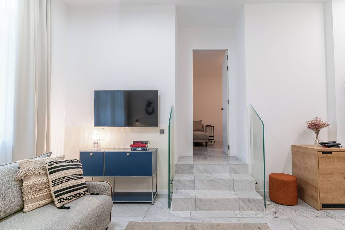 Ein modernes Wohnzimmer mit einer Couch, einem Fernseher, einem blauen Schrank und einem Holzkasten.