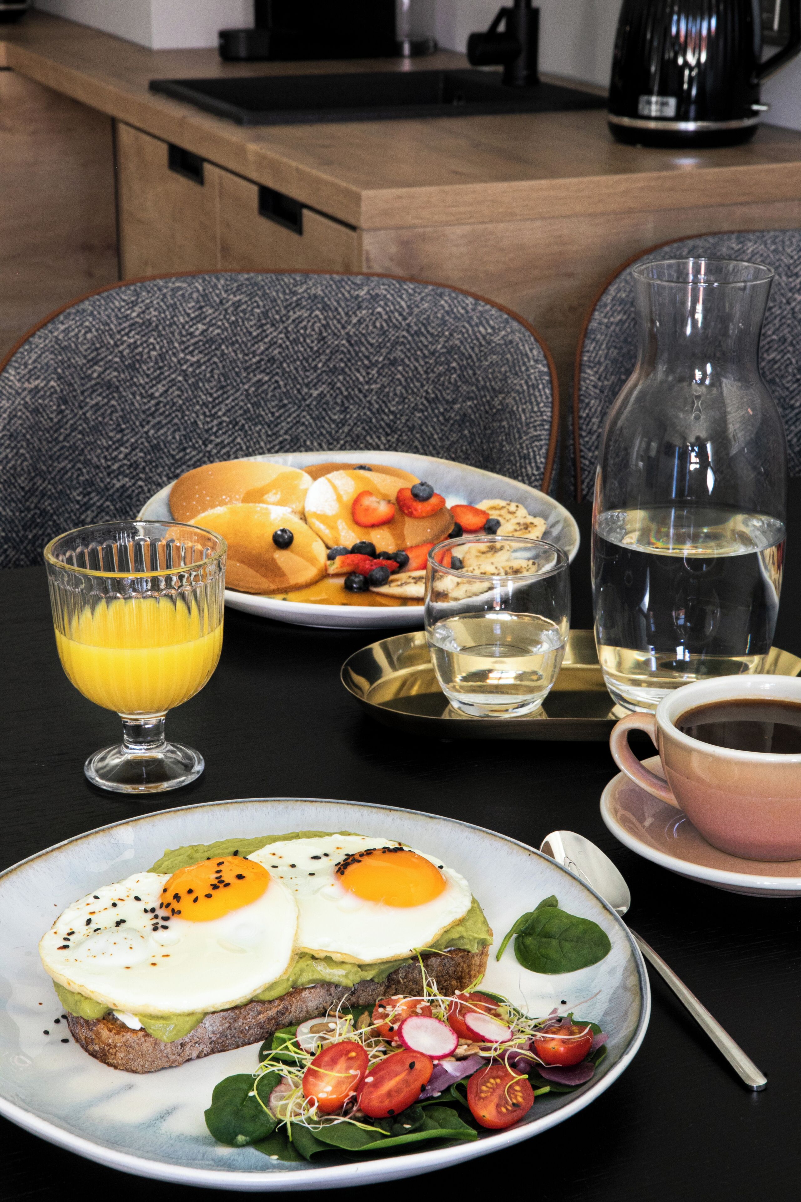 Uma mesa de café da manhã com uma pilha de panquecas, um copo de suco de laranja, uma xícara de café e um copo de água em um bandejão.