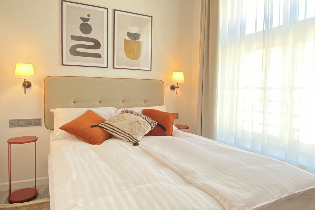 Een hotelkamer met een groot bed, twee wandlampen en twee kunstwerken in lijsten erboven.