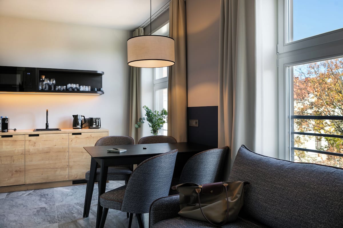 Ein modernes Zimmer mit Esstisch, Stühlen, einer Couch, einem an der Wand montierten Fernseher und einem großen Fenster mit Blick auf Bäume.