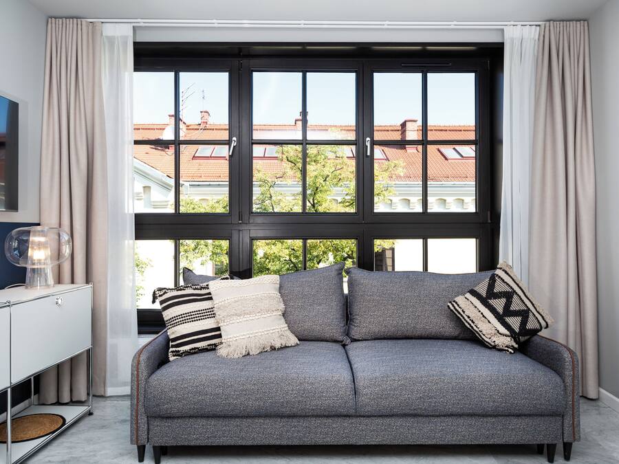 A modern living room with a grey sofa, a TV on the left, and a large window with curtains.