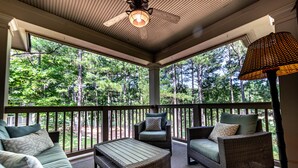 A covered porch with wicker furniture, a ceiling fan, and a view of a forest.