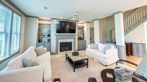 A modern living room with a fireplace, two white sofas, a coffee table, and a TV mounted above the fireplace.