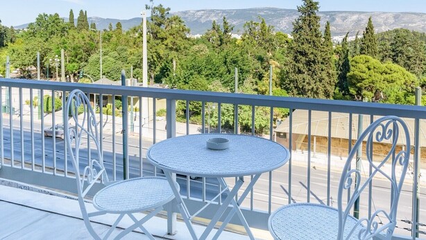 A balcony with a round table and two chairs, overlooking a street and greenery.