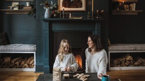 A cozy living room with a fireplace, a mantel decorated with candles and books, and a child playing with wooden blocks. - Historic Luxury Downtown Victorian home with Hot Tub, Ocean and Harbour Views (St. John's)