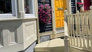 A house with a yellow door, white railings, and a small porch. - Historic Luxury Downtown Victorian home with Hot Tub, Ocean and Harbour Views (St. John's)