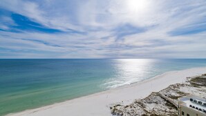 Ein Strand mit blauem Himmel und ruhiger See. Auf der rechten Seite befindet sich ein Gebäude mit flachem Dach und Klimaanlagen.