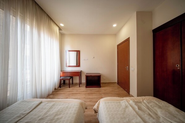 A hotel room with two beds, a desk, a chair, a wardrobe, and a mirror.