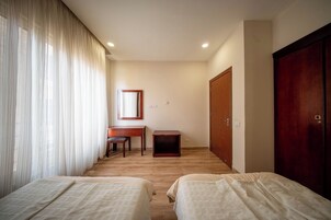 Habitación de hotel con dos camas, un escritorio, una silla, un armario y un espejo.