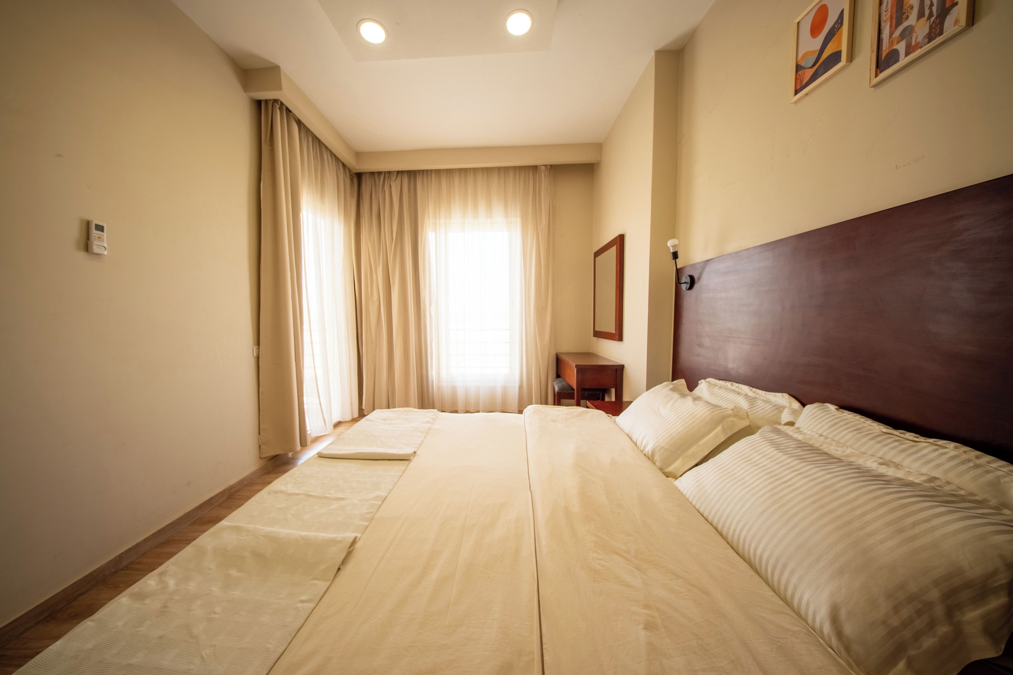 Ein Hotelzimmer mit einem großen Bett, einem Nachttisch, einem Spiegel und einem Fenster mit Vorhängen.