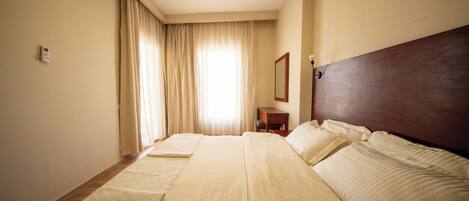 Una habitación de hotel con una cama grande, una mesita de noche, un espejo y una ventana con cortinas.