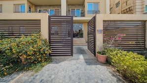 A gated entrance to a multi-story residential building with a paved pathway leading to the entrance. - The Home (6th of October City)