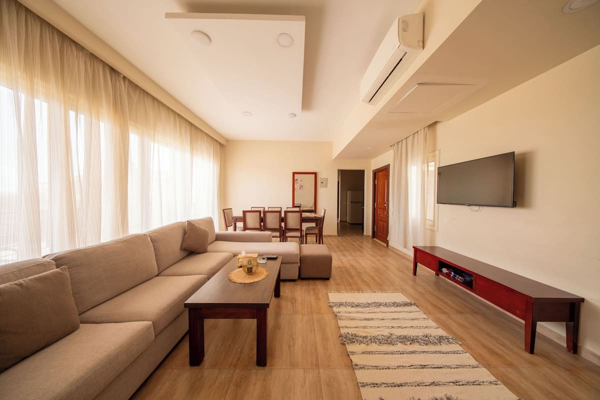 A modern living room with a sofa, coffee table, TV, and a dining area.