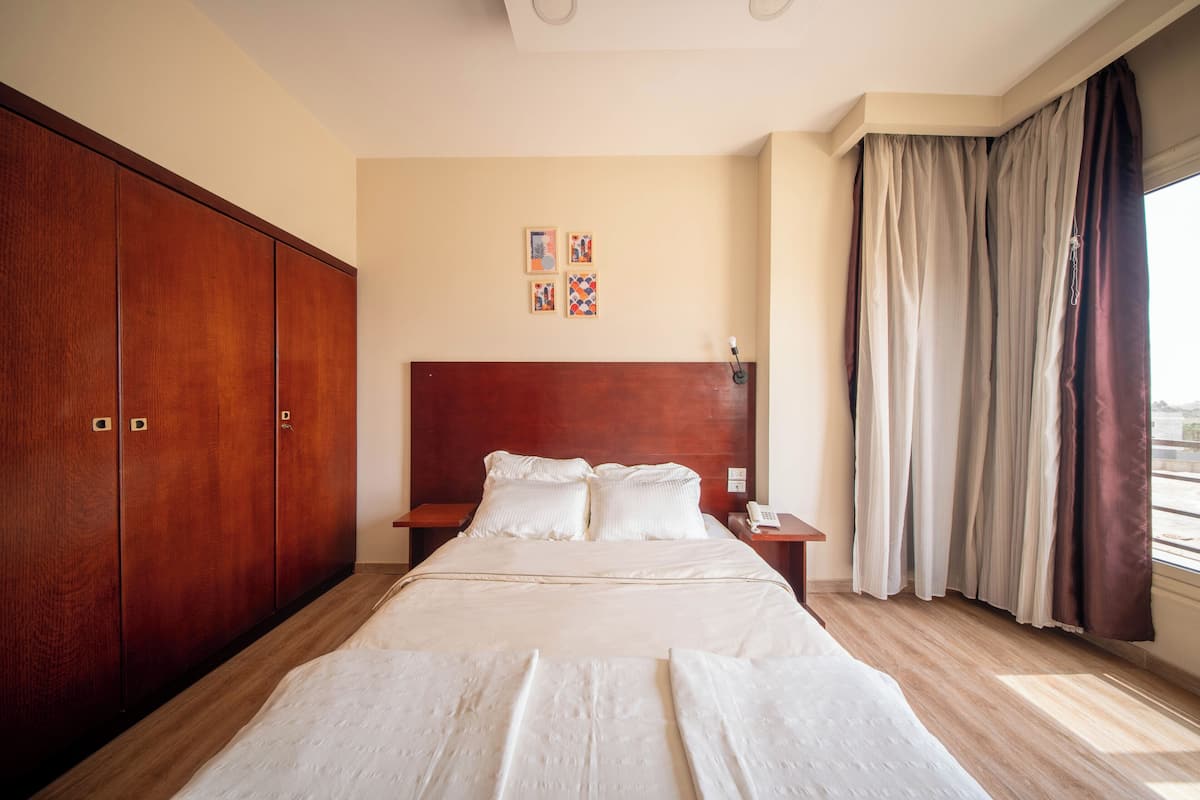 A hotel room with a large bed, wooden wardrobe, bedside tables, and a window with curtains.