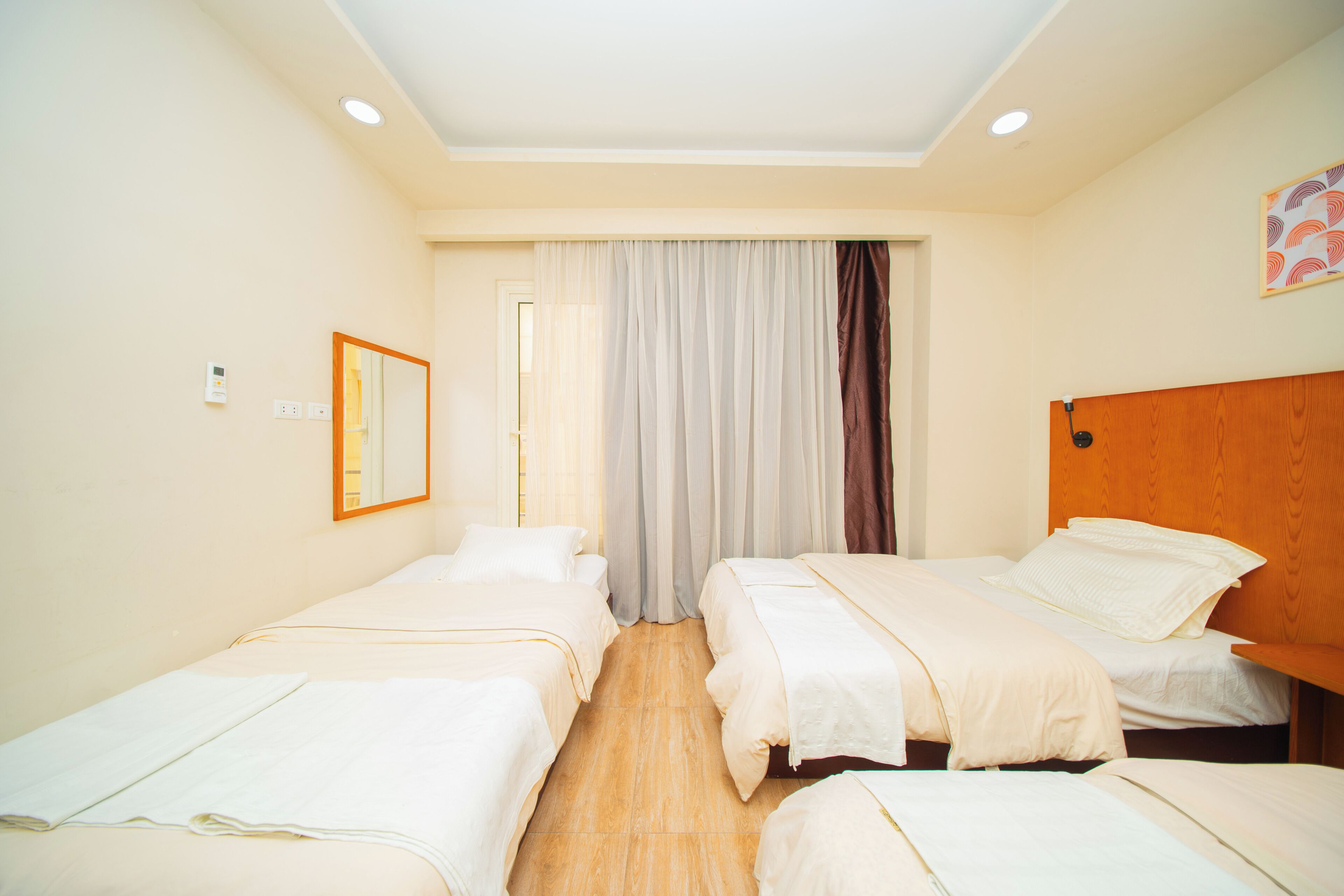 A hotel room with two single beds, a wooden headboard, a mirror, and a window with curtains.