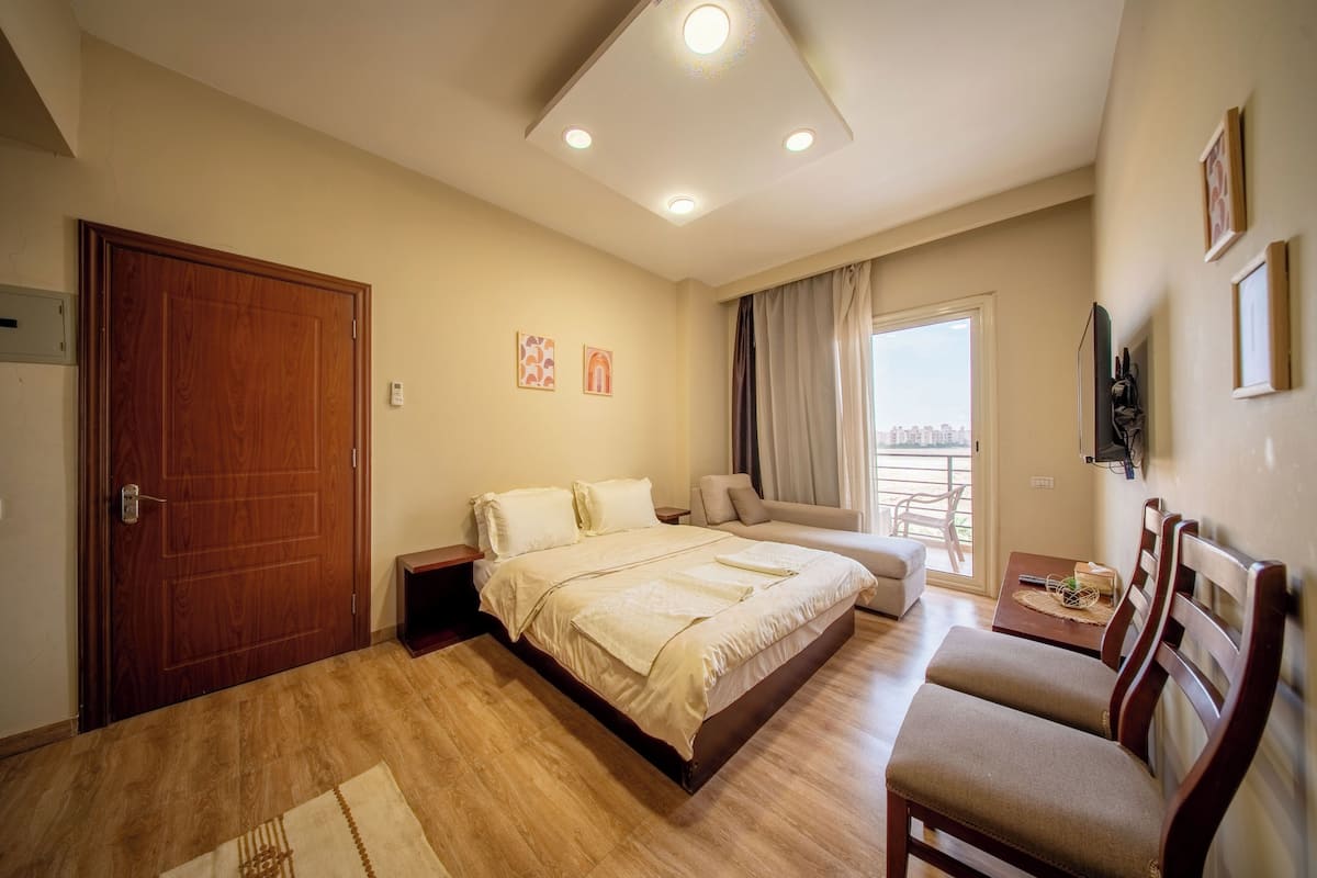 A hotel room with a bed, a sofa, a TV, and a balcony with a city view.