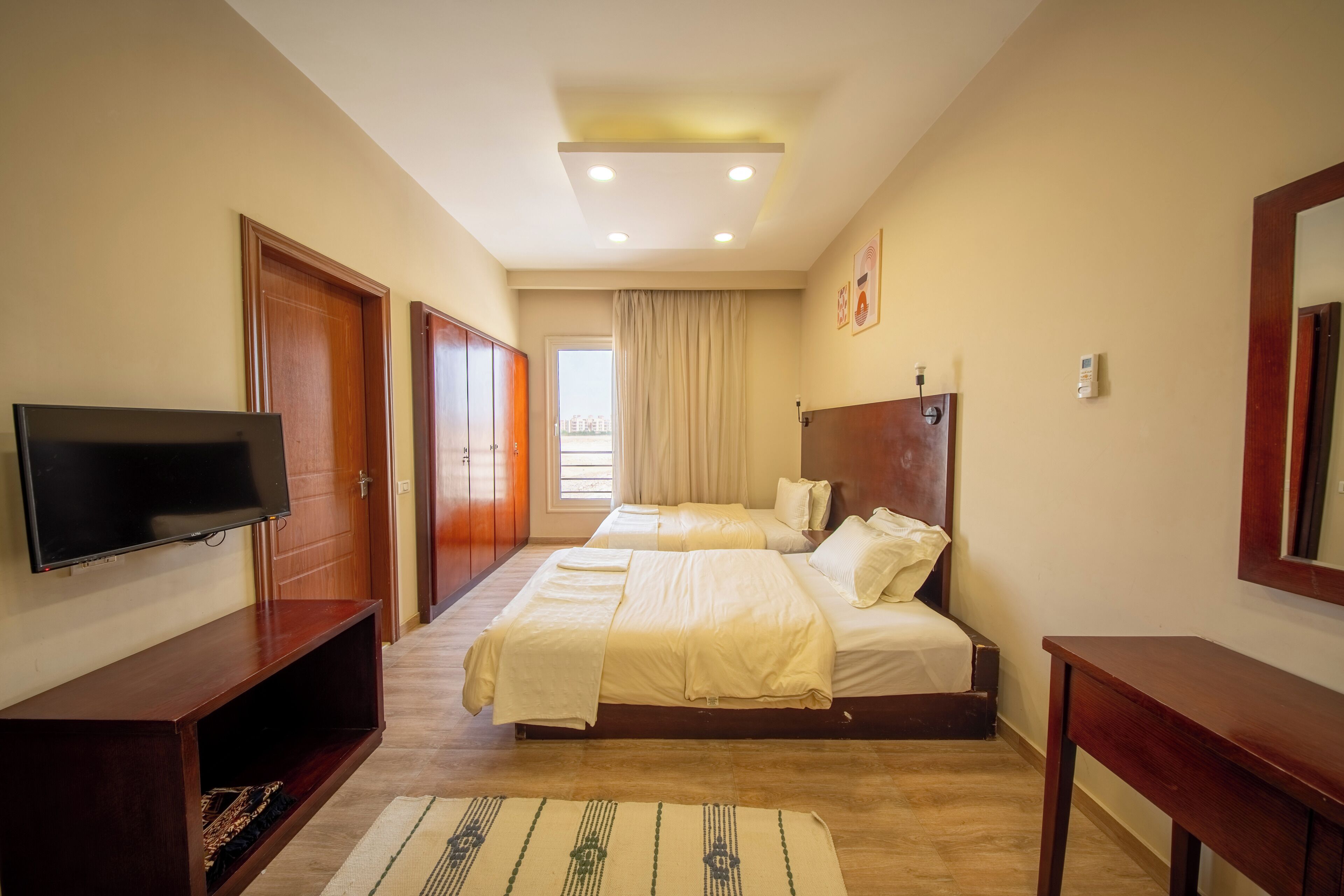A hotel room with a TV, two beds, a wooden dresser, and a large window.