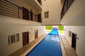 A pool area with a long, narrow pool, a covered walkway, and a view of a green lawn.