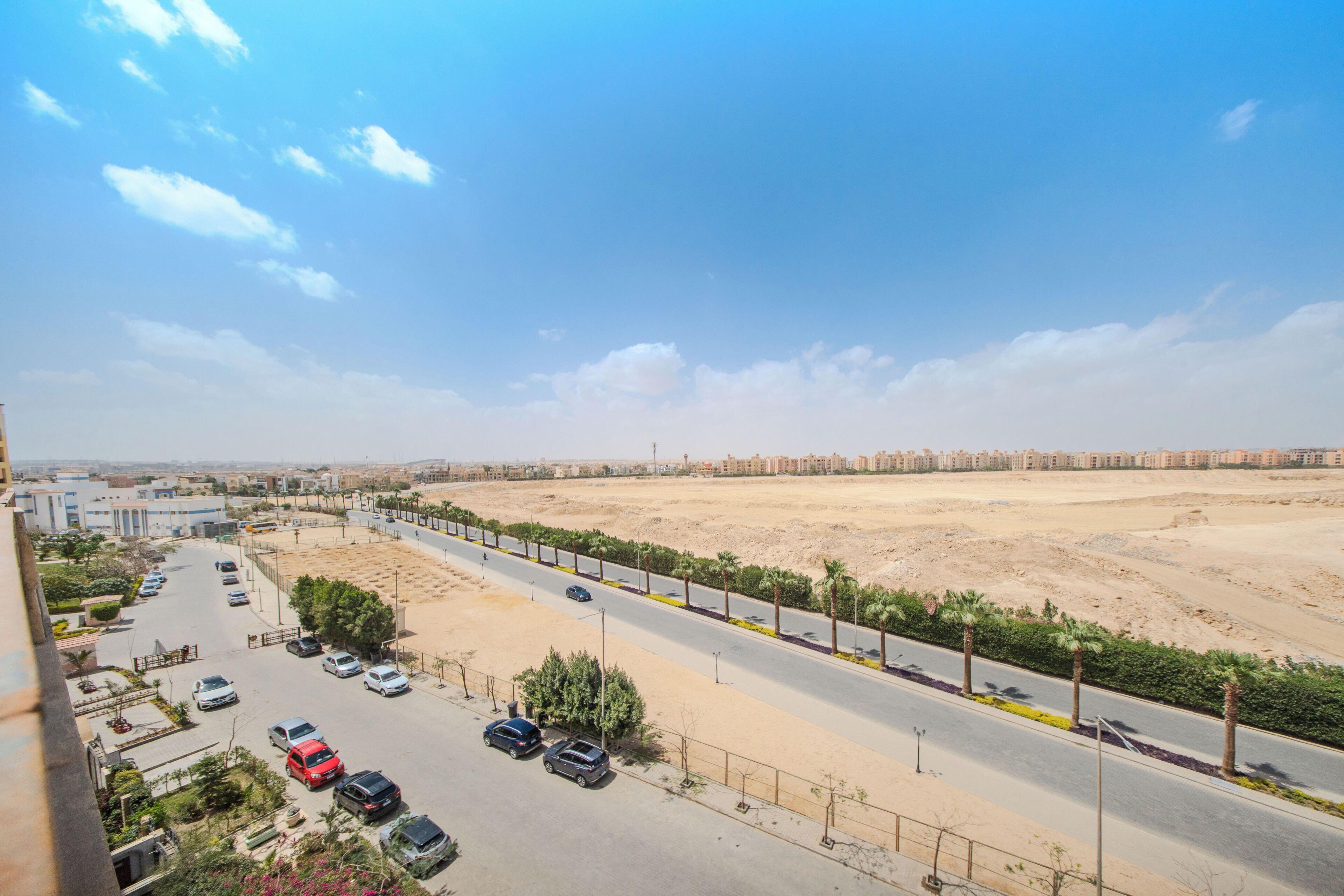 A road with parked cars, a clear sky, and distant buildings.