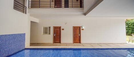 A swimming pool with a tiled floor, a balcony with a railing, and two wooden doors.