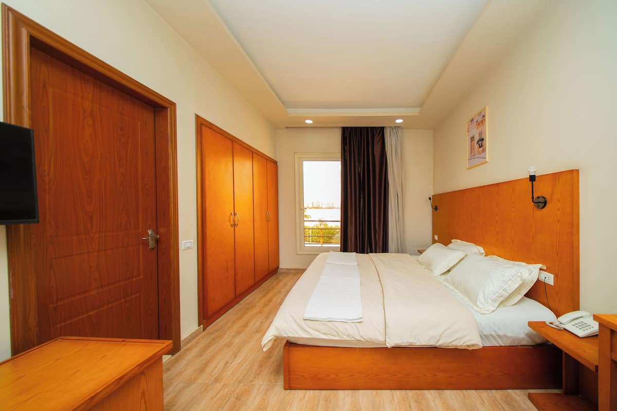 A hotel room with a wooden bed, a bedside table with a phone, a wooden wardrobe, and a television on the left wall.