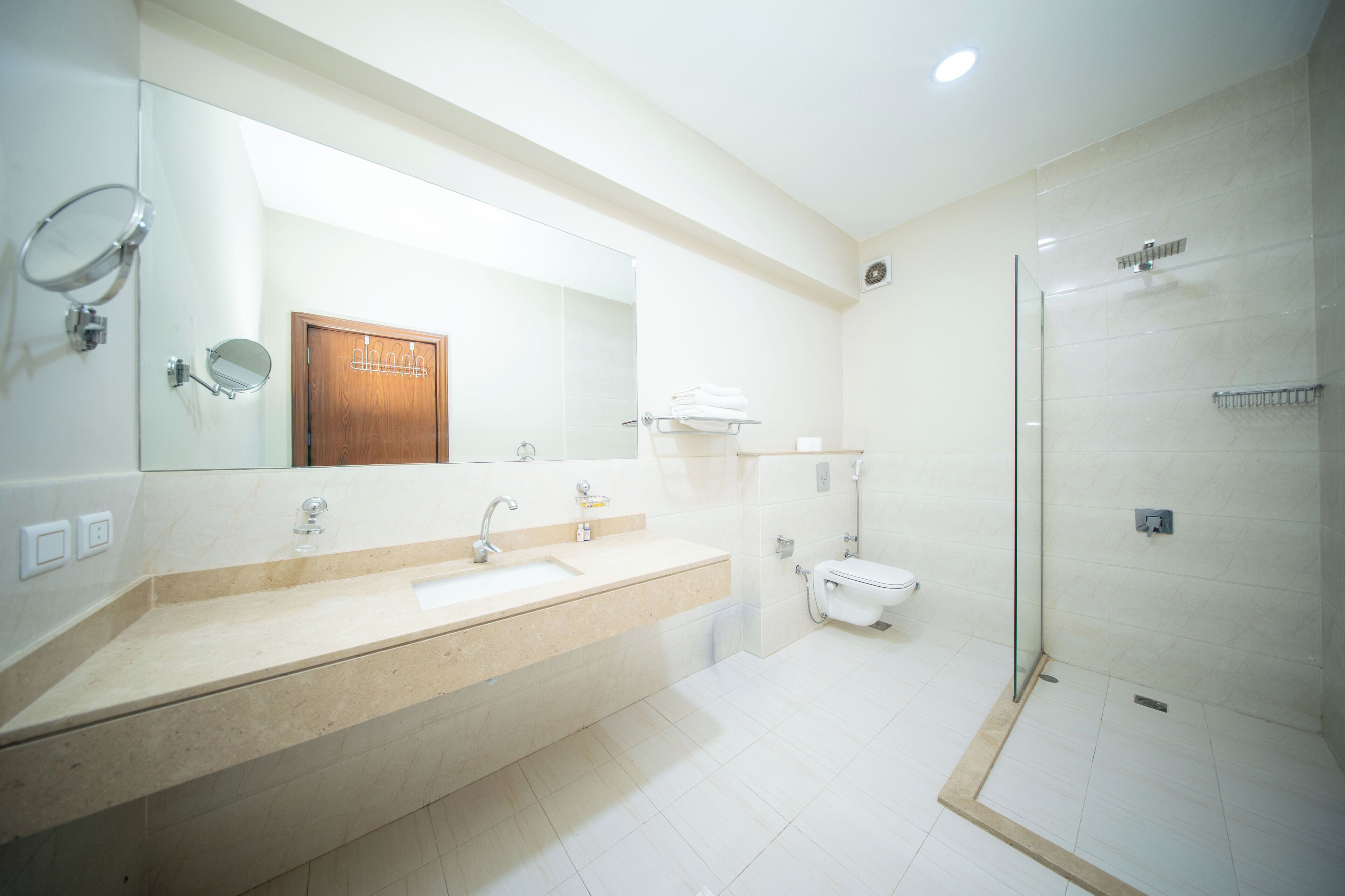 Un baño moderno con un espejo grande, un lavamanos, un inodoro y una ducha con cerramiento de vidrio.
