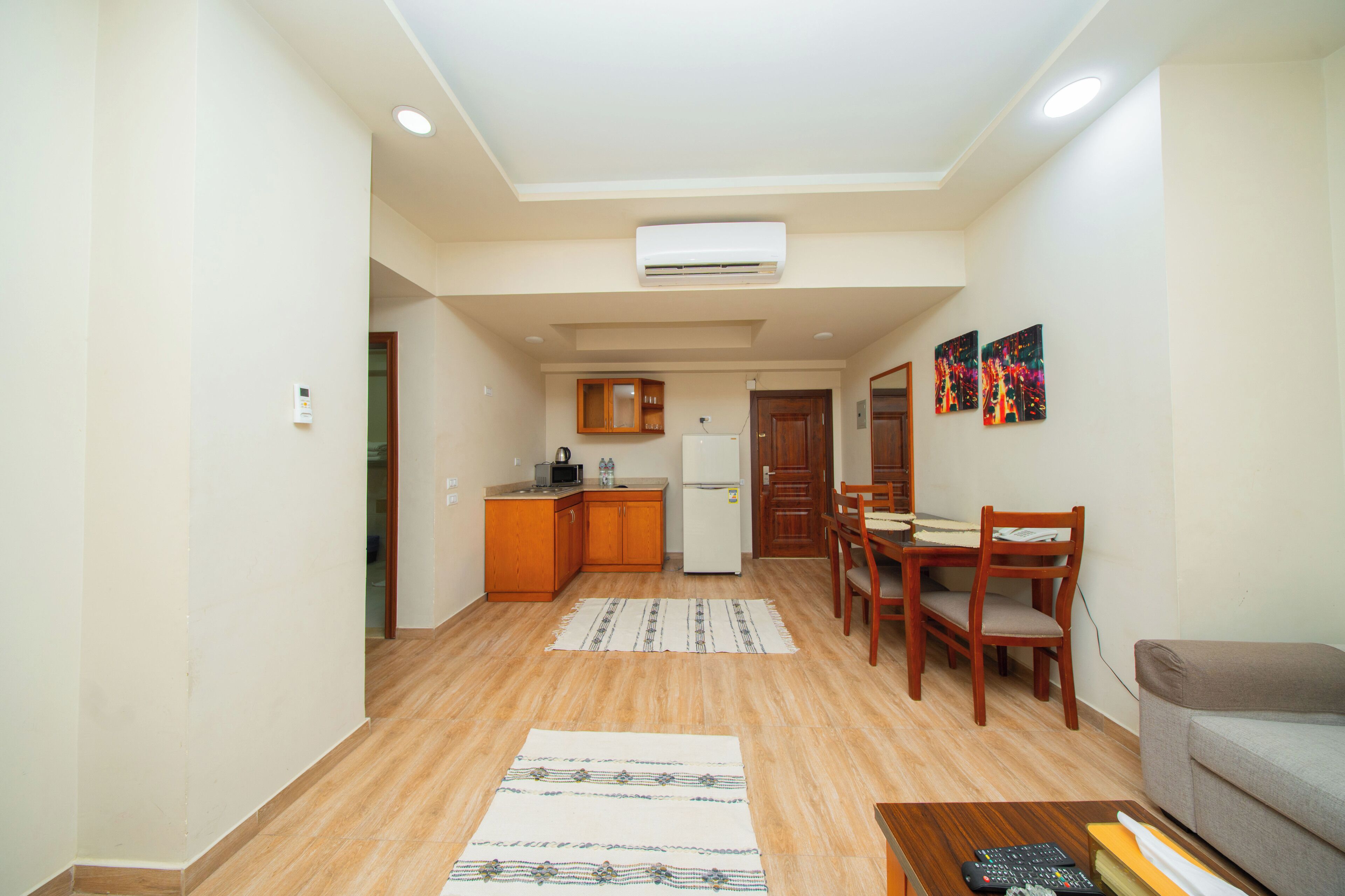 A living room with a sofa, a coffee table, a dining table with chairs, a kitchen area with cabinets and appliances, and a hallway.