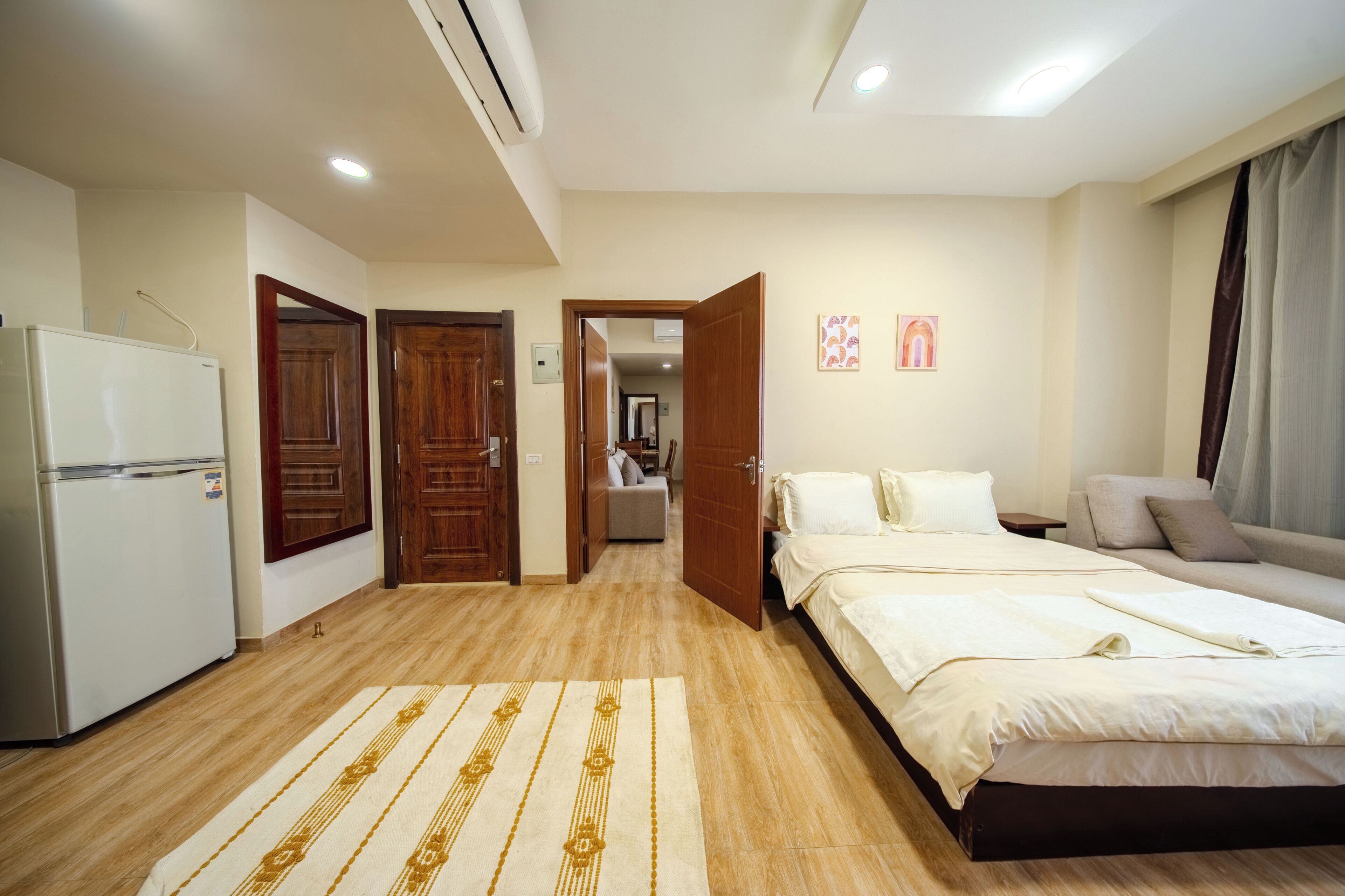 A bedroom with a bed, bedside tables, a refrigerator, and a wooden door.