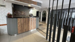 A reception area with a wooden counter, a wall-mounted display of items, and a tiled floor. - Elit Otel (Antalya)