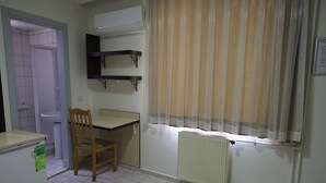 A small, clean room with a desk, chair, radiator, and a window with curtains. - Elit Otel (Antalya)