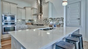 Een moderne keuken met witte kasten, een groot eiland met krukken, een roestvrijstalen afzuigkap en een decoratieve spatwand.
