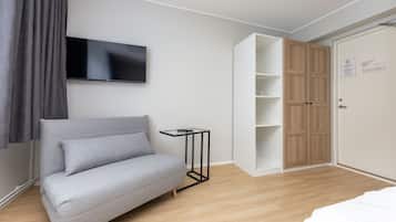 Un dormitorio moderno con un sofá gris, un televisor montado en la pared, un armario de madera y una pequeña mesita de noche negra.