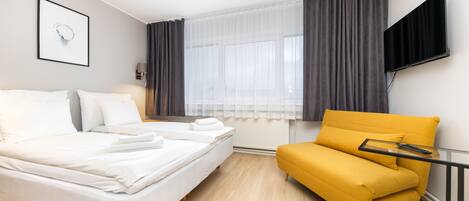 Una habitación de hotel moderna con una cama, un sofá, un televisor y un ventanal con cortinas.