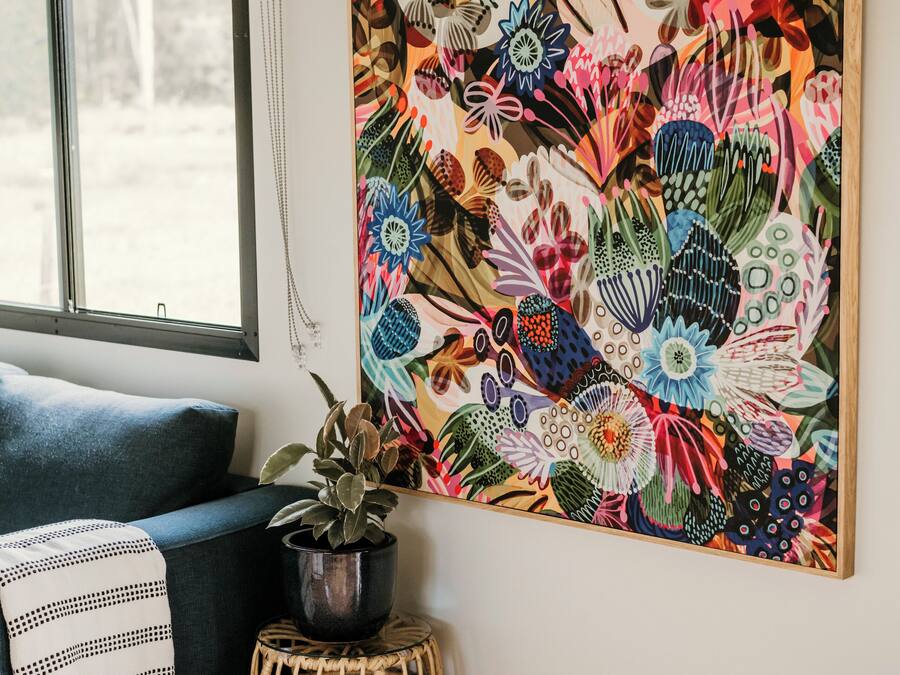 Une pièce décorée d’une grande œuvre d’art florale au mur, avec un canapé bleu, une petite plante en pot et une table d’appoint en osier.