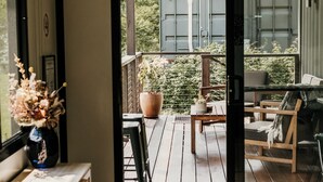A wooden deck with a table and chairs, a potted plant, and a view of a building with a garage door. - Contained in Nimbin (Nimbin)