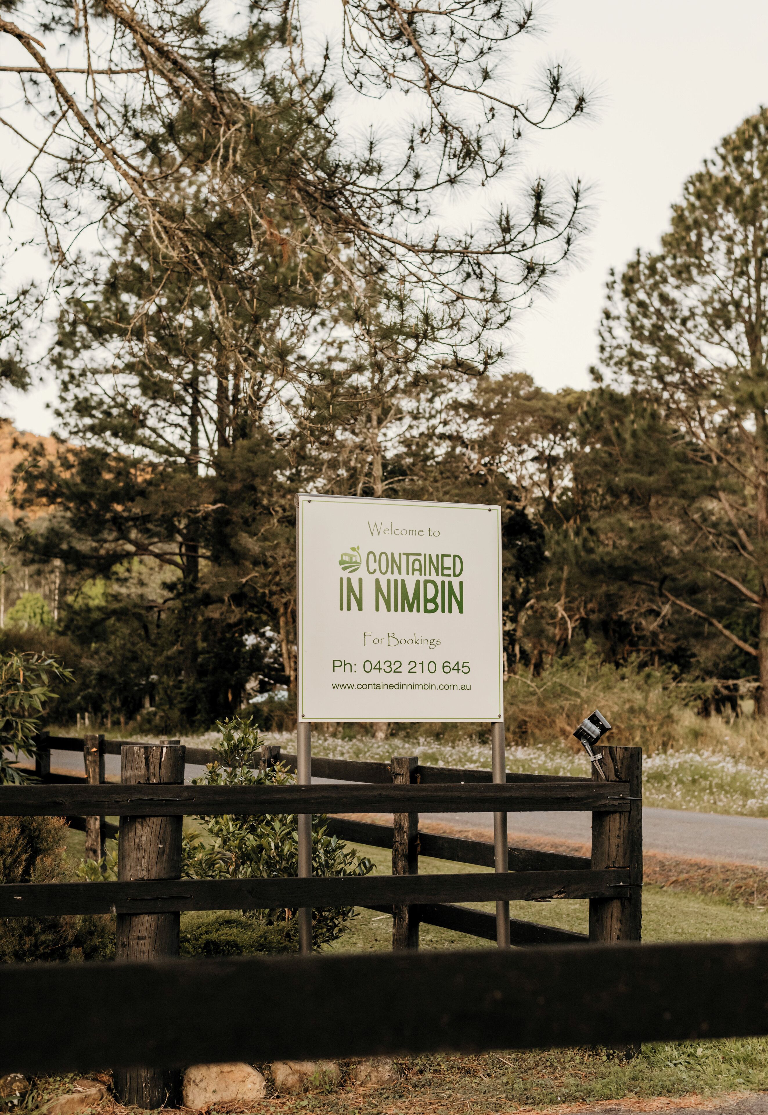 A sign welcoming visitors to a contained area in Nimbin, with contact information for bookings.
