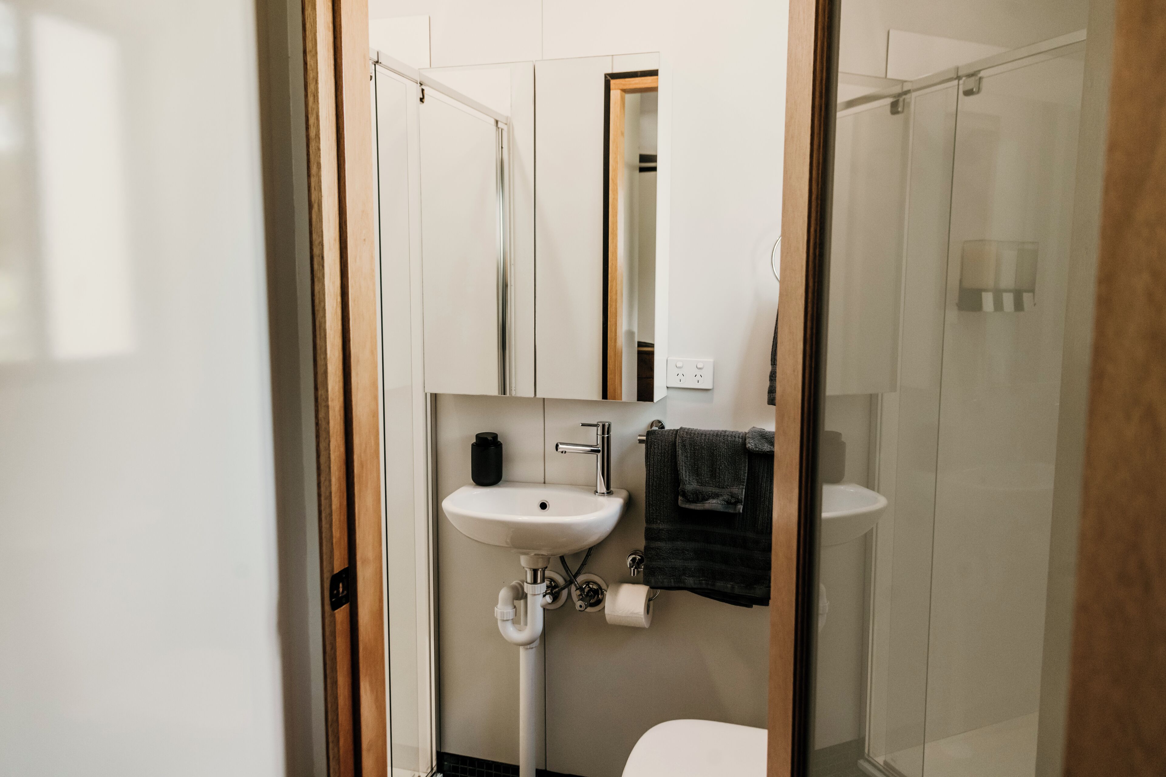 A compact bathroom with a white sink, a mirror, a towel, and a glass shower enclosure.