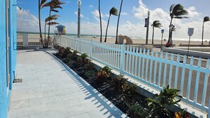 Un paseo marítimo con valla blanca, palmeras y vistas a la playa y al océano.