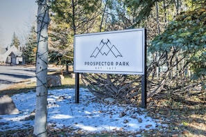 Schild für Prospector Park mit Berglogo, gegründet 1977, umgeben von Bäumen und Schnee.