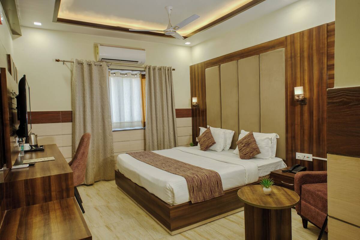 A hotel room with a large bed, a desk, a chair, a small table, and a ceiling fan.