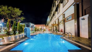 Una piscina con bordo piastrellato, circondata da piante in vaso e un edificio dal design moderno.